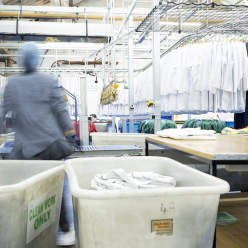 Women working in an industrial laundry, stood in front of barrows with workwear behind her.