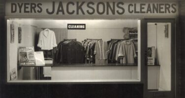 Black and white image of Jacksons front window with clothes hanging on rails inside.