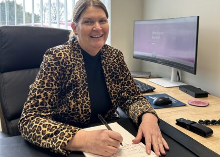 Dr Melanie Mackinder sat at a desk, looking at the camera.