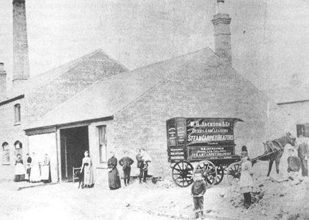 old building with a horse pulling a cart with Jacksons branding on and people stood outside.