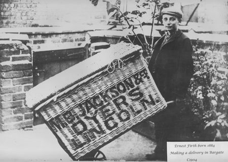 Young boy pushing a large wicker basket on wheels with Jacksons advertising on it from 1800s